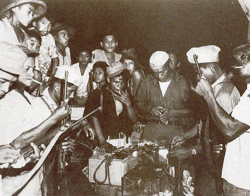 group of Filipino guerrillas clustered around an illegal radio, listening for news of the war.